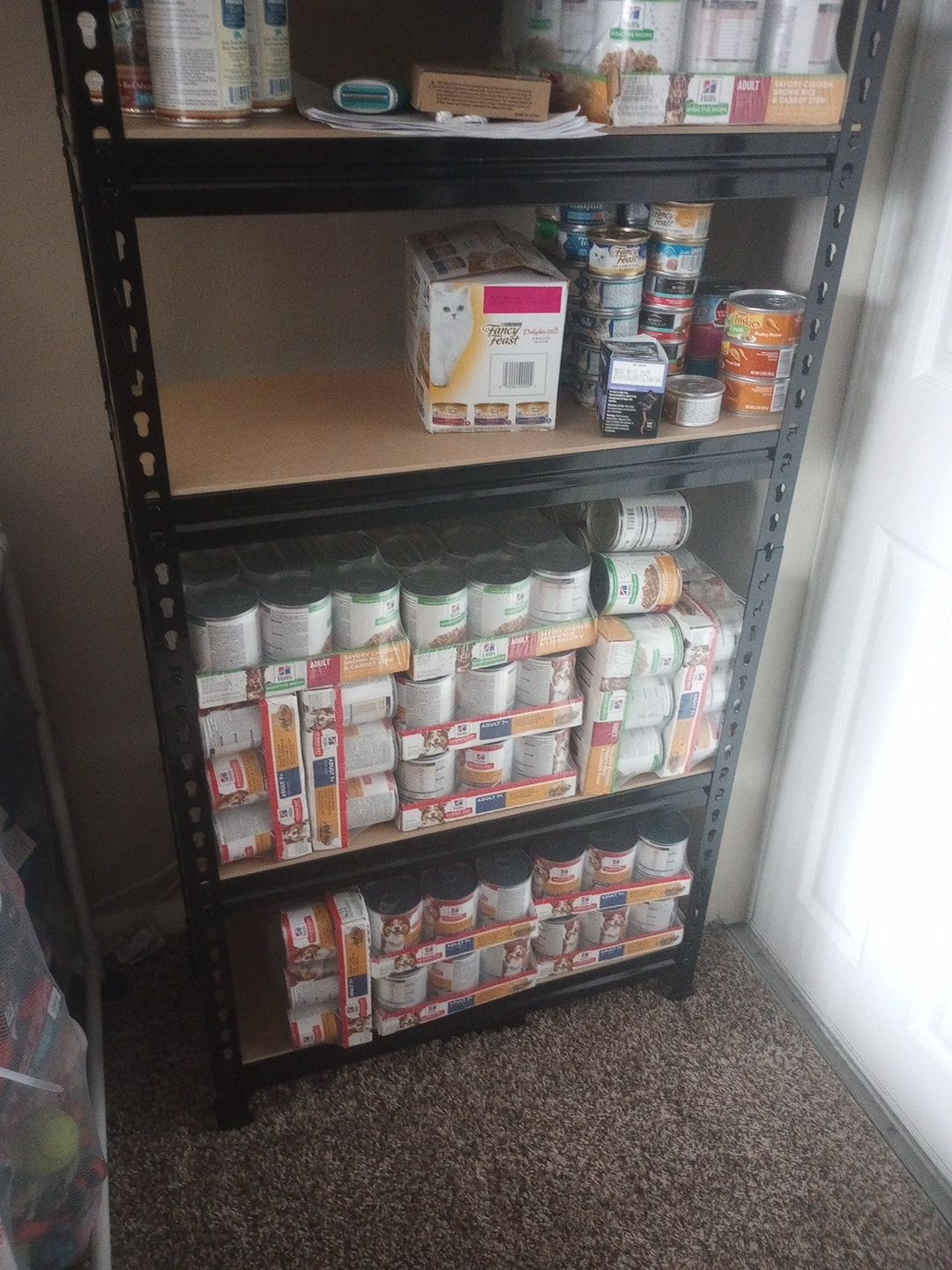 A tall metal shelf at home, filled with cans of dog and cat food.